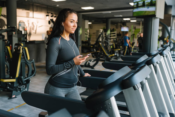 Portrait of Fitness woman running on treadmill in gym listening to music.exercising concept.fitness and healthy lifestyle. - Fotografie, Obrázek