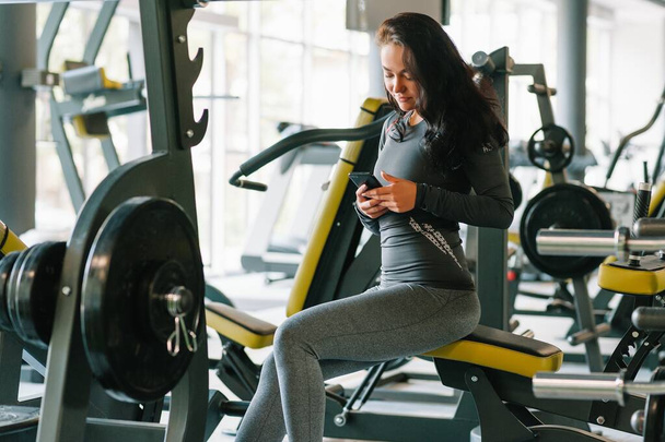 Gorgeous young woman texting and social networking while in a gym - Фото, изображение