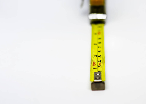 zatahovací žlutá kovová měřicí páska izolovaná na bílém pozadí. Měření vyjádřená v centimetrech a stopách. Stavební měřicí přístroj - Fotografie, Obrázek