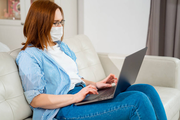 female in medical mask works with computer online. - Photo, Image