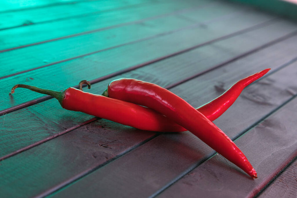 Red chili pepper on a wooden table made of dark slats. Red on black. Popular spice. Refined taste. The repeating diagonal lines of the boards. Burning fiery taste. - Foto, imagen