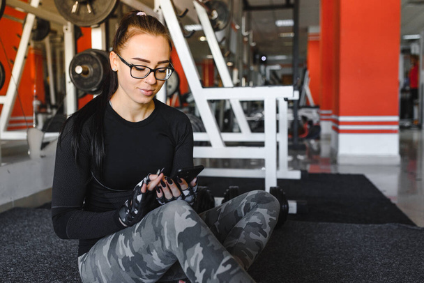 Portrait of a cheerful sports woman using smartphone in fitness gym - Fotó, kép