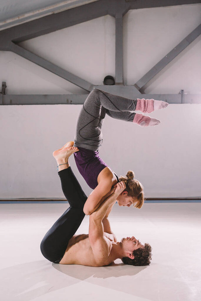 The theme of Acroyoga and Yoga Poses. Acroyogis practicing. with studio Backlight. the man Base holds in the Static poses a woman Flyer in the top above herself in her arms. Position scorpion. - Foto, Imagem