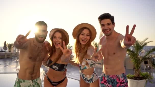 Quattro giovani amici attraenti felici che mostrano i pollici verso l'alto gesti e guardando la fotocamera a bordo piscina
 - Filmati, video