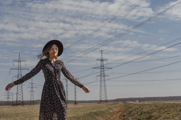 Schöne Mädchen in einem Kleid auf dem Land. Vor dem Hintergrund eines Feldes und Hochspannungsleitungen zwischen Weizen. Blauer Himmel und Modell - Foto, Bild