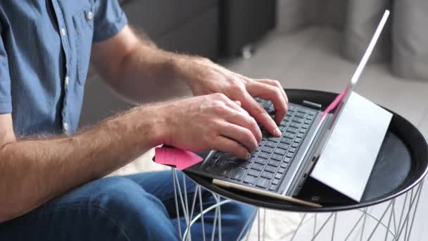 Jeune homme confiant assis à son canapé à la maison, ouvre et commence à utiliser un ordinateur portable. Consept de travail à domicile en ligne. Quarantaine virale
 - Séquence, vidéo