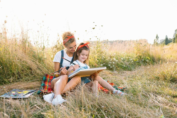 mother teaches daughter paint in park. Sunny nature, mom and daughter paint a picture in a park , painting a Little Child, Child Creativity. Mother's Day - Фото, изображение
