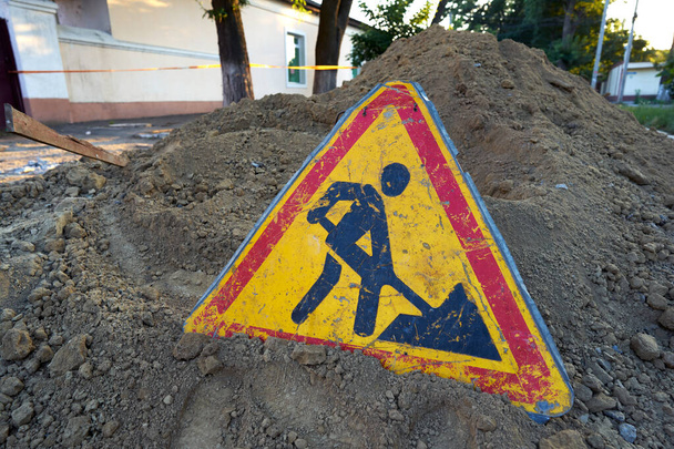Señal de trabajo en carretera colocada en una pila de tierra excavada en medio de una carretera que está siendo reparada
 - Foto, imagen