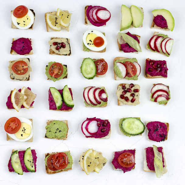 σετ διαφορετικά σάντουιτς μπρουσκέτα με χούμους τεύτλων, γκουακαμόλε, διαφορετικά λαχανικά. χορτοφαγική ιδέα για φαγητό. καλοκαιρινό σνακ. food patern σε λευκό φόντο - Φωτογραφία, εικόνα