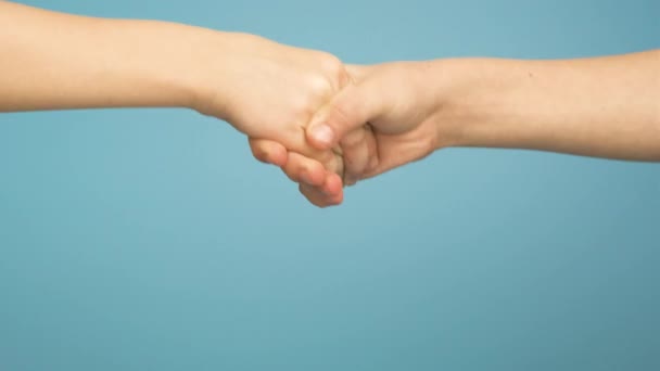 Großaufnahme von zwei Kinderhänden beim gemeinsamen Händeschütteln isoliert auf blauem Hintergrund. - Filmmaterial, Video