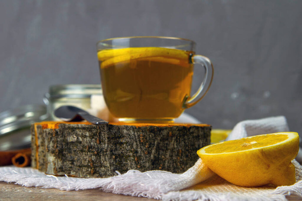 Skleněný průhledný šálek s mátovým čajem stojí na dřevěném stojanu, vedle cukrové misky s kostkami cukru, plátky citronu a lžičkou. - Fotografie, Obrázek