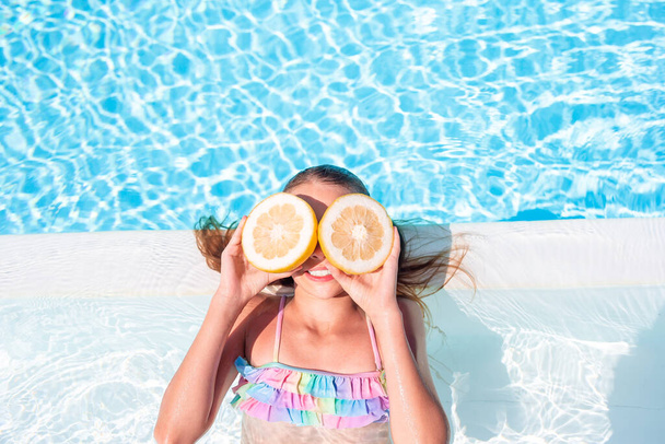 Klein meisje met helften citruscitroenen in zwembad - Foto, afbeelding