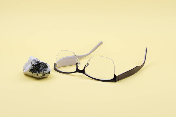 Glasses and moonstone on a yellow background. - Photo, Image