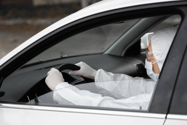 Man in protective suit, medical mask and rubber gloves for protect from bacteria and virus is planning to drive. Protective mask while quarantine, world pandemic, covid 19, coronavirus, infection. - Foto, afbeelding