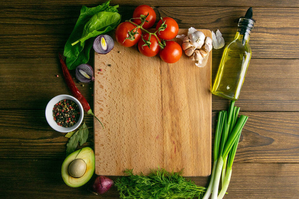 Wooden board with clear space. Around tomato and dill, olive oil, spice, peper, avocado, green onion, spinac and garlic. Top views. - Photo, Image
