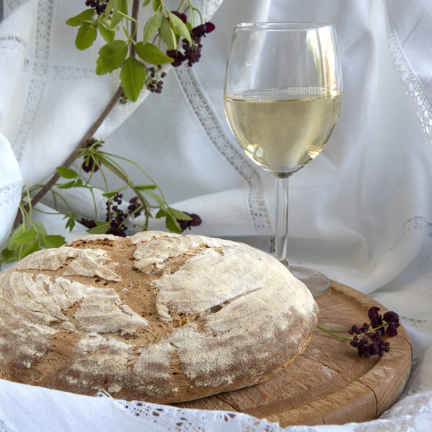 Ένα καρβέλι ψωμί ολικής αλέσεως σε λευκή πετσέτα κουζίνας με πράσινα φύλλα και λουλούδια - Φωτογραφία, εικόνα