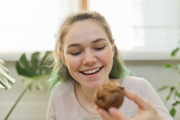 Teenage girl leads culinary vlog for teenagers, girl shows freshly baked chocolate muffin, looks at webcam, tells recipe - Фото, изображение