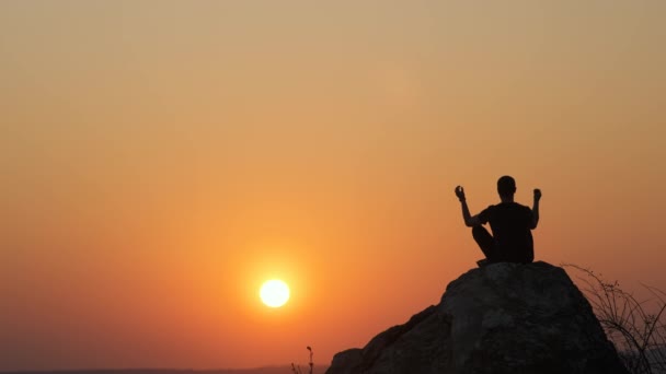 Silueta muže, který sedí sám na velkém kameni při západu slunce v horách. Muž turista těší pohled na vysoké skály ve večerní přírodě. Cestovní ruch, cestování a zdravý životní styl. - Záběry, video