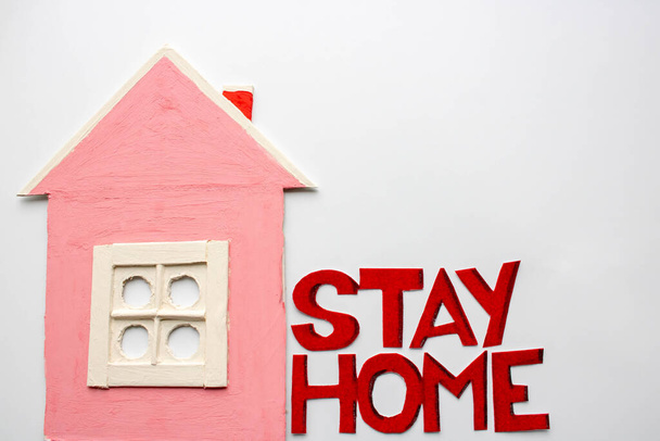 Ein kleines rosafarbenes Haus neben den Worten, ein Aufruf, zu Hause zu bleiben. Warnung vor dem Covid-19 Coronavirus oder einer Epidemie. - Foto, Bild