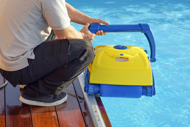 Un limpiador de piscinas sostiene un limpiador de robots. Limpiador de piscinas durante su trabajo. Trabajador del hotel caucásico limpiando la piscina - Foto, imagen