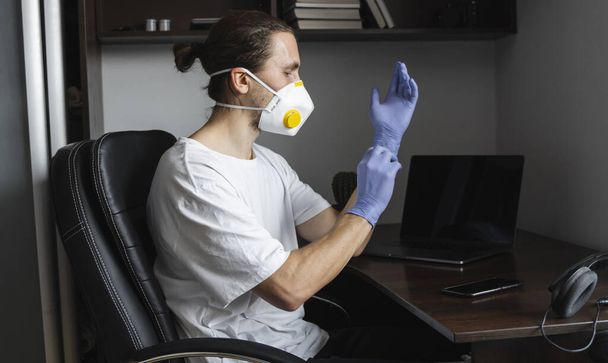 Man in medical mask is wears rubber gloves at his working place at home during quarantine. Designer, artist, architect, businessman at remote work in a pandemic covid. - Fotografie, Obrázek