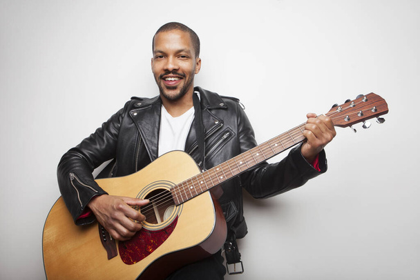 Handsome African man playing guitar wearing leather jacket isolated on white background. - 写真・画像
