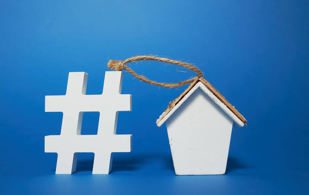 Fique em casa conceito. Símbolo de hashtag e estatueta de uma casa de madeira em um fundo azul. Área vazia para texto
. - Foto, Imagem