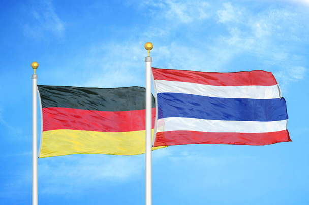 Německo a Thajsko dvě vlajky na vlajkových stožárech a modrá oblačná obloha pozadí - Fotografie, Obrázek