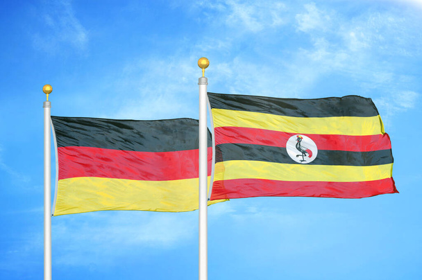 Almanya ve Uganda bayrak direkleri ve mavi bulutlu arka planda iki bayrak - Fotoğraf, Görsel