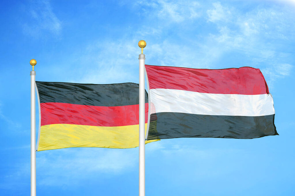 Германия и Йемен два флага на флагштоках и голубом облачном фоне неба
 - Фото, изображение