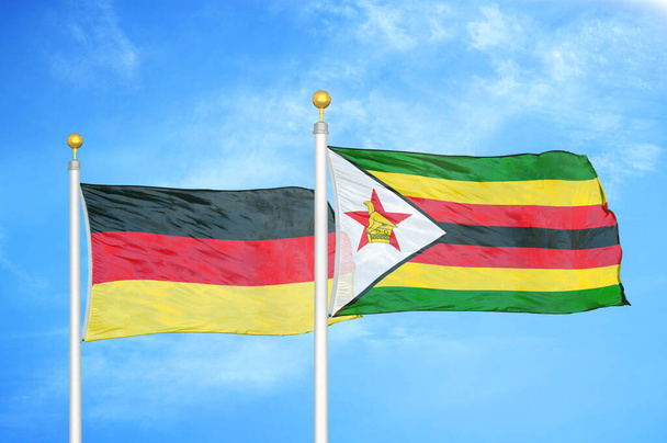 Německo a Zimbabwe dvě vlajky na vlajkových stožárech a modrá oblačná obloha pozadí - Fotografie, Obrázek