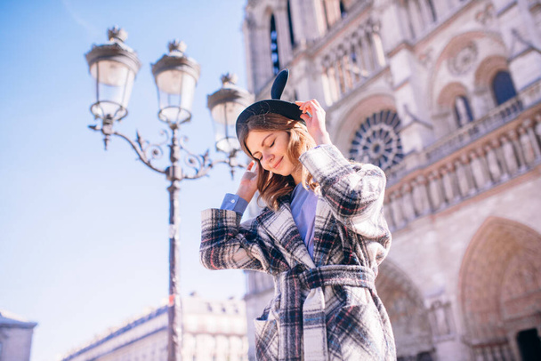 beautiful girl in a mikimaus hat in a beautiful coat on the background of the Parisian Cathedral of Notre Dame - Φωτογραφία, εικόνα