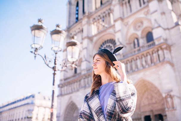 beautiful girl in a mikimaus hat in a beautiful coat on the background of the Parisian Cathedral of Notre Dame - Foto, Bild