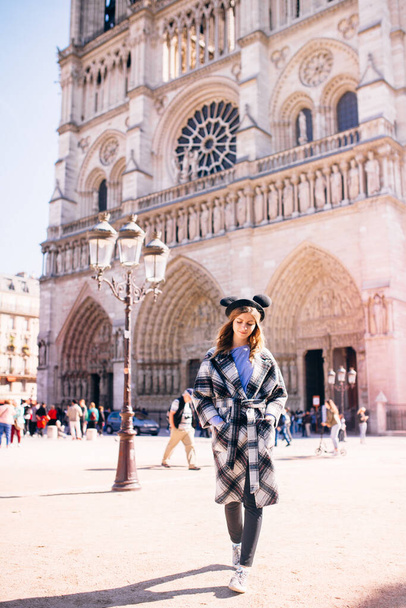 beautiful girl in a mikimaus hat in a beautiful coat on the background of the Parisian Cathedral of Notre Dame - Fotografie, Obrázek