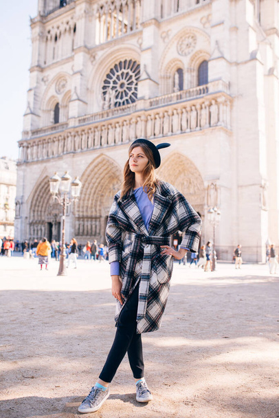 beautiful girl in a mikimaus hat in a beautiful coat on the background of the Parisian Cathedral of Notre Dame - Photo, Image