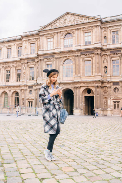 A girl in a beautiful coat stands near the Louvre. Concept of visiting France and historical buildings. - Fotografie, Obrázek
