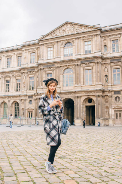 A girl in a beautiful coat stands near the Louvre. Concept of visiting France and historical buildings. - Valokuva, kuva