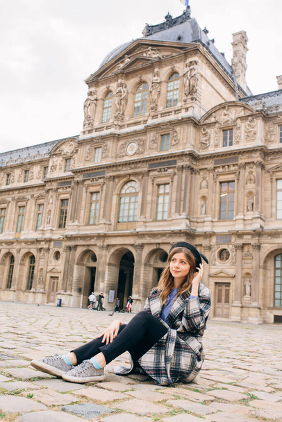 A girl in a beautiful coat stands near the Louvre. Concept of visiting France and historical buildings. - Foto, Imagen