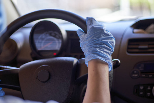 Młoda kobieta w masce chirurgicznej i rękawiczkach jeżdżąca samochodem podczas pandemii koronawirusowej. Samica kierowcy w sprzęcie ochronnym, zapobiegająca zakażeniu wirusem covid-19 - Zdjęcie, obraz