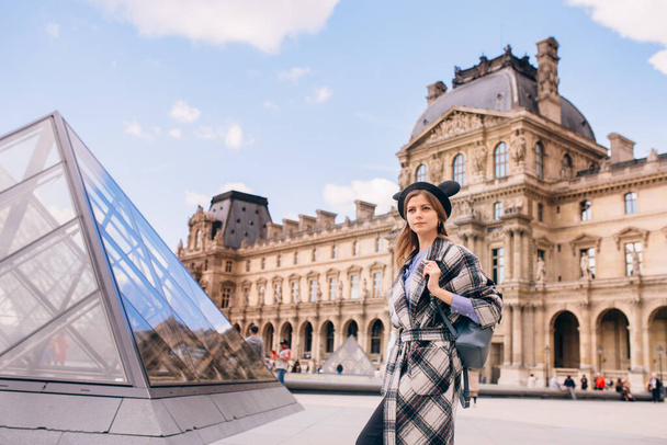 A girl in a beautiful coat stands near the Louvre. Concept of visiting France and historical buildings. - Φωτογραφία, εικόνα