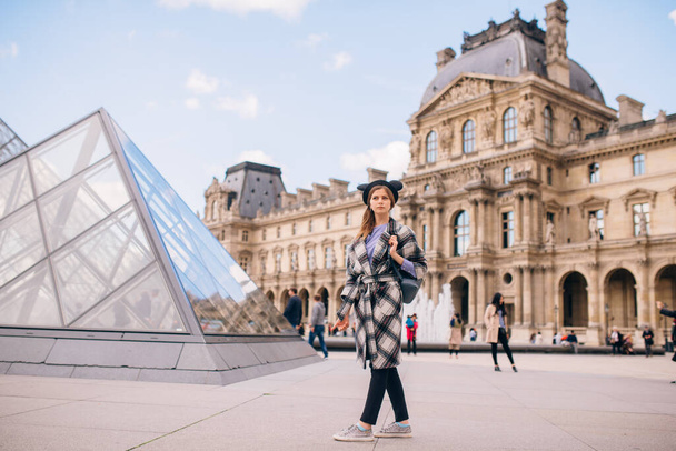 A girl in a beautiful coat stands near the Louvre. Concept of visiting France and historical buildings. - Фото, изображение