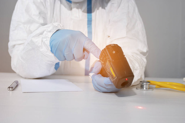Il dottore in una tuta biologica protettiva e guanti aggiusta il termometro infrarosso
 - Foto, immagini