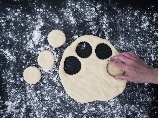 Dłoń kobiety kroi ciasto i robi bułeczki na łupkowym tle. widok z góry - Zdjęcie, obraz