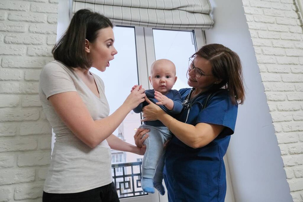 Női orvos vizsgálja kisgyermek. A gyerekorvos karba vette a babát, beszélt az anyjával, és együtt nevettek. Gyermekek gyógyítása, gondozása és egészsége legfeljebb egy évig - Fotó, kép