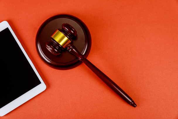 Espaço de trabalho para advogado com tela em branco tablet digital e juízes martelo de madeira no fundo vermelho
 - Foto, Imagem