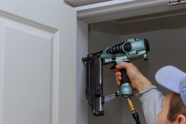 Pracownik stolarski przy instalacji drzwi z użyciem pistoletu pneumatycznego - Zdjęcie, obraz