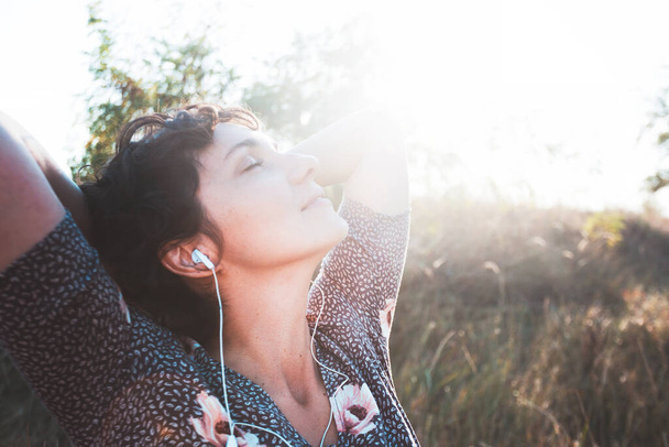 happy smiling girl in headphones listens to music on a sunset background. photo out of focu - Fotó, kép