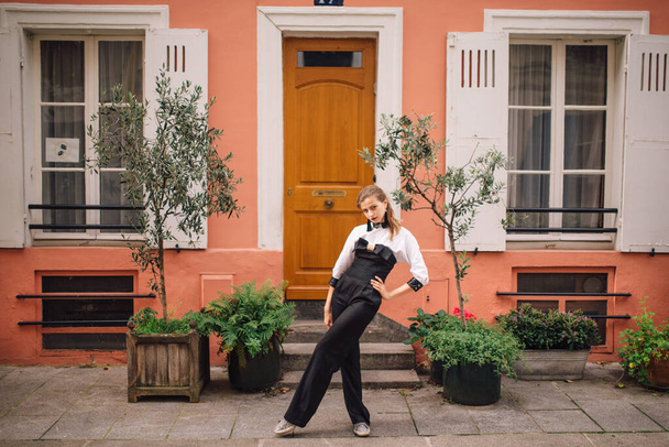 Una bella giovane donna in tuta nera alla moda si trova su una strada parigina con case colorate e luminose.Francia
 - Foto, immagini