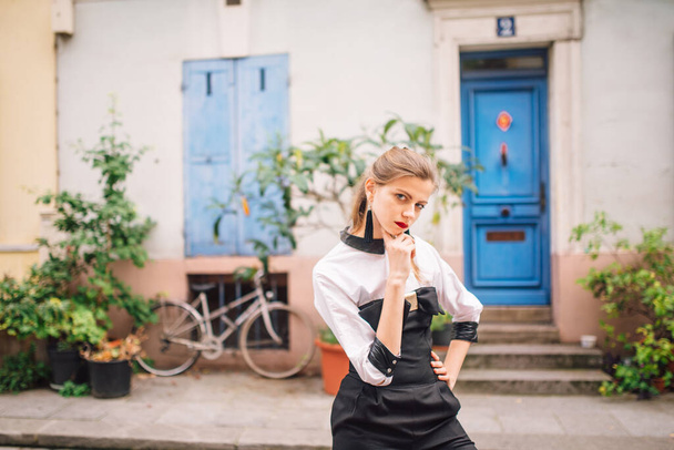 A beautiful young woman in a black fashionable jumpsuit stands on a Parisian street with colorful bright houses.France - Zdjęcie, obraz