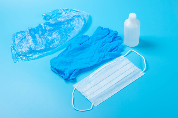 Одноразовая медицинская маска, антисептическая и латексная перчатка на светло-голубой поверхности. Обувные чехлы на синем фоне
 - Фото, изображение